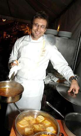 Male chef holding lid to show what is cooking in large pot